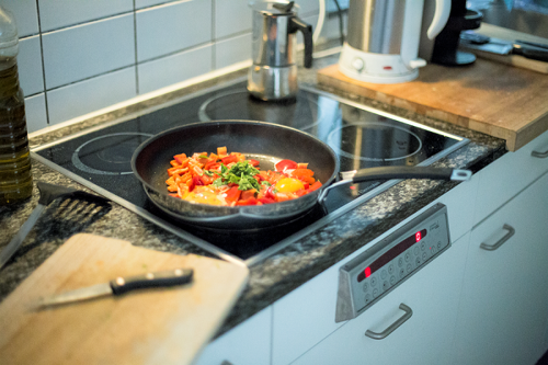 Frying pan on a hob with eggs and vegetables in it