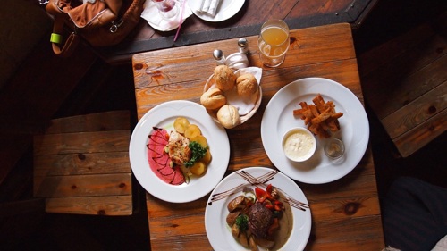 Photo of four plates of food on a wooden table with a drink